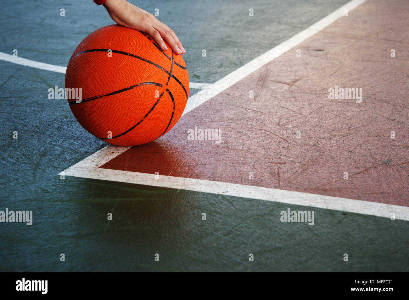 Basket-ball orange unique avec femme main de joueur sur la texture vert rouge fond plancher gymnase sport Banque D'Images