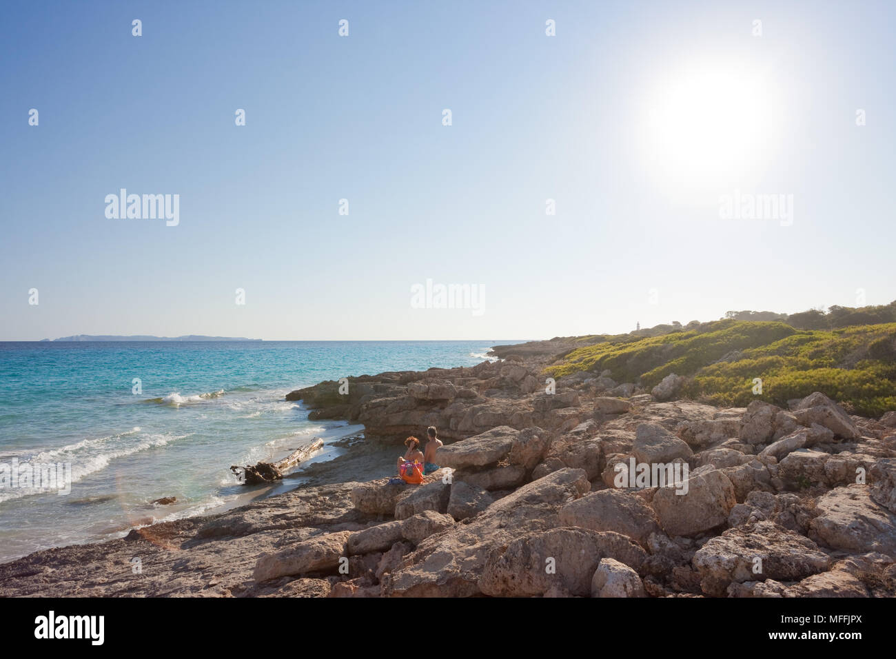 Cap de Ses Salines, Majorque, Espagne - AOÛT 2016 - Les touristes assis à la plage solitaire de Ses Salines pour le coucher du soleil Banque D'Images