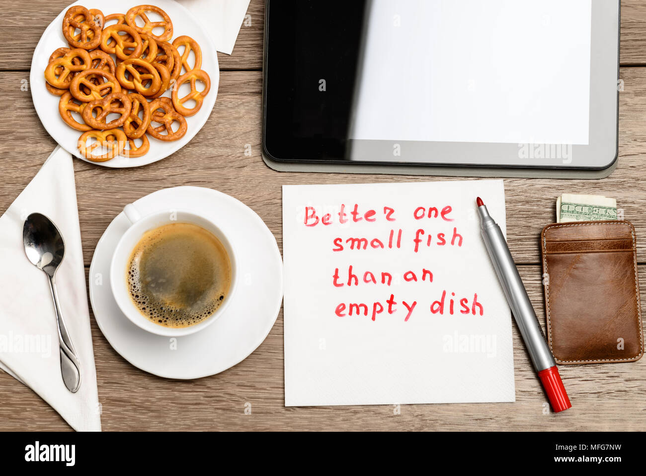 Proverbe message serviette sur table en bois avec du café, de la nourriture et PC tablette mieux un petit poisson d'un plat vide Banque D'Images
