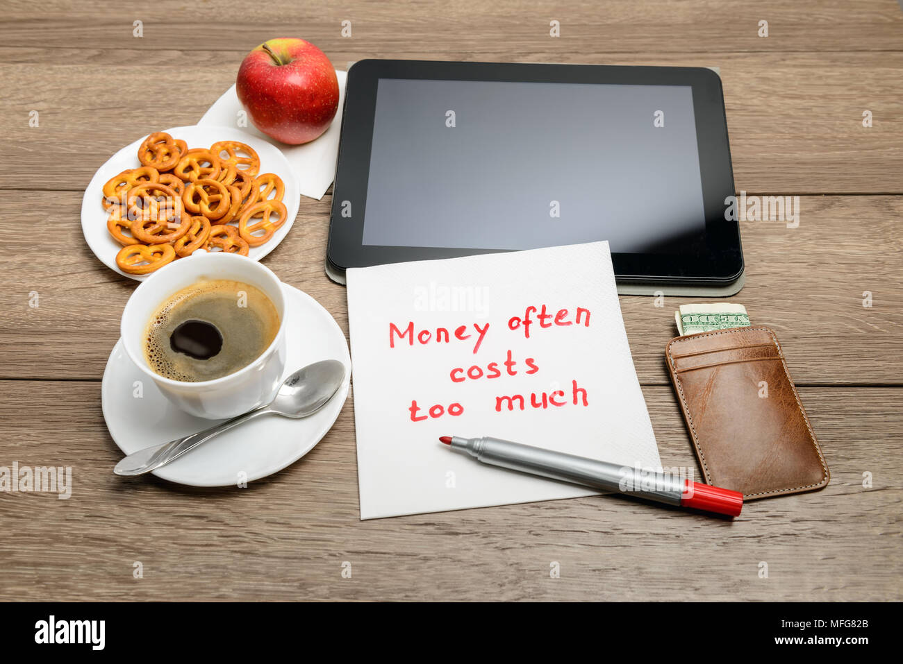 Message de l'écriture de serviette sur proverbe table en bois avec du café, de la nourriture et tablet PC de l'argent coûte souvent trop cher Banque D'Images