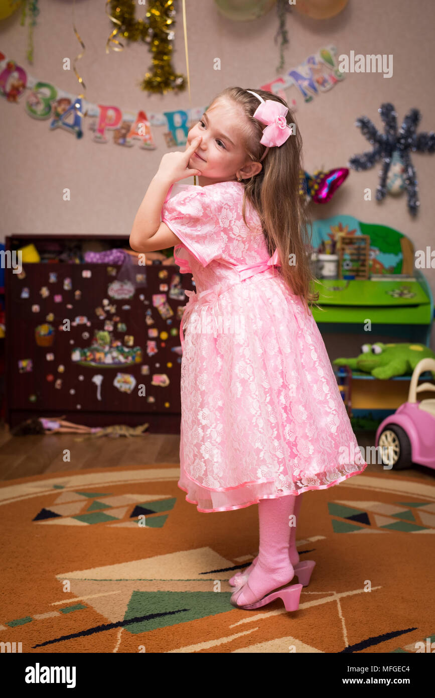 Petite fille dans une belle robe rose de poser dans une chambre d'enfants Banque D'Images