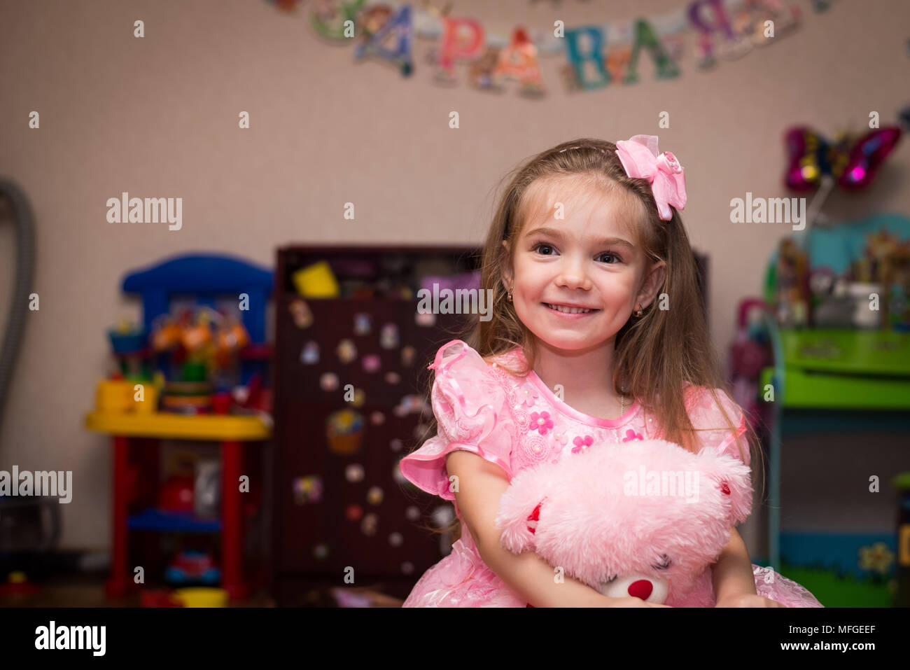 Petite fille dans une belle robe rose sourit dans la chambre des enfants Banque D'Images