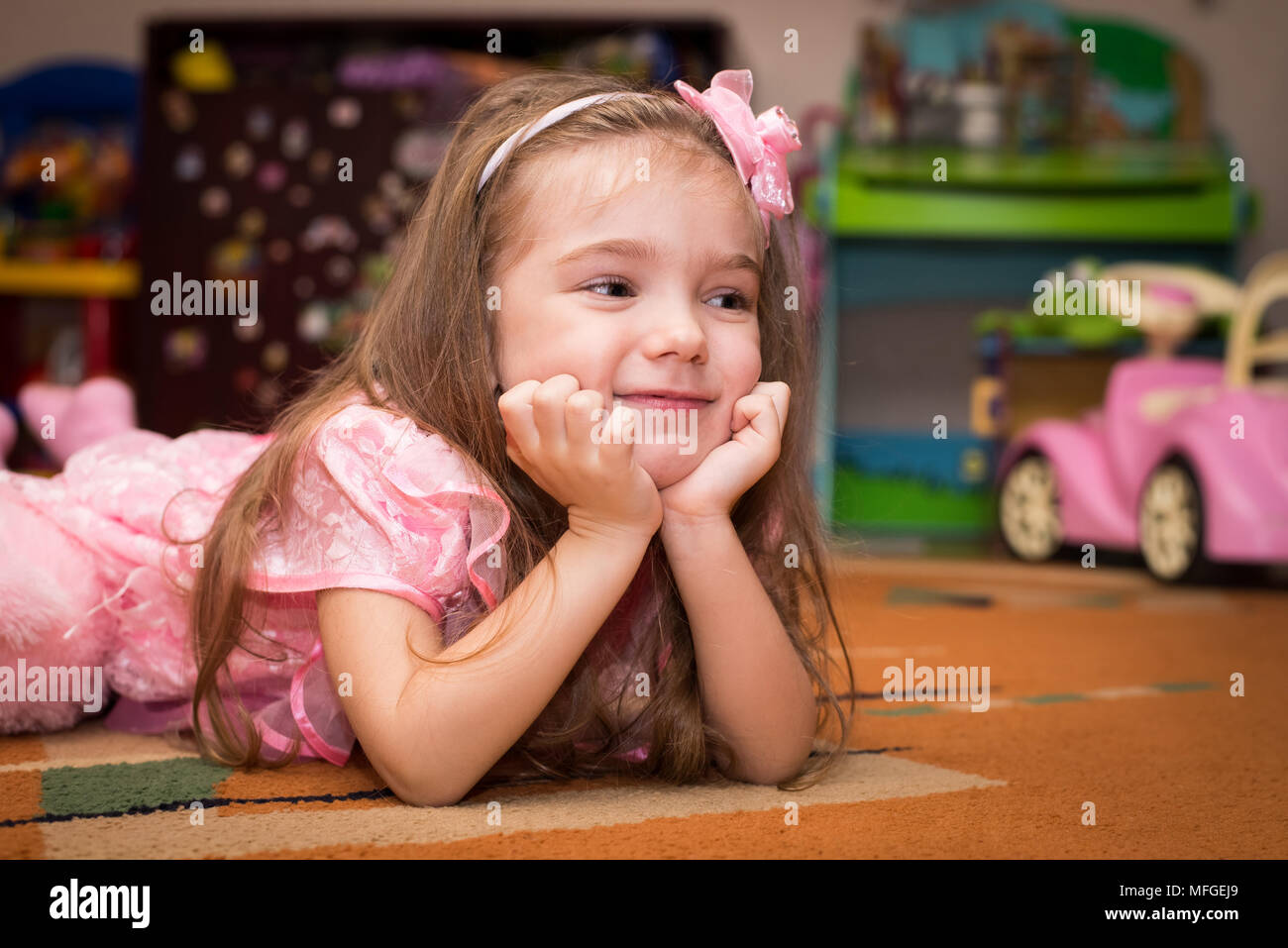 Petite fille dans une robe rose se trouve sur le sol avec un jouet Banque D'Images