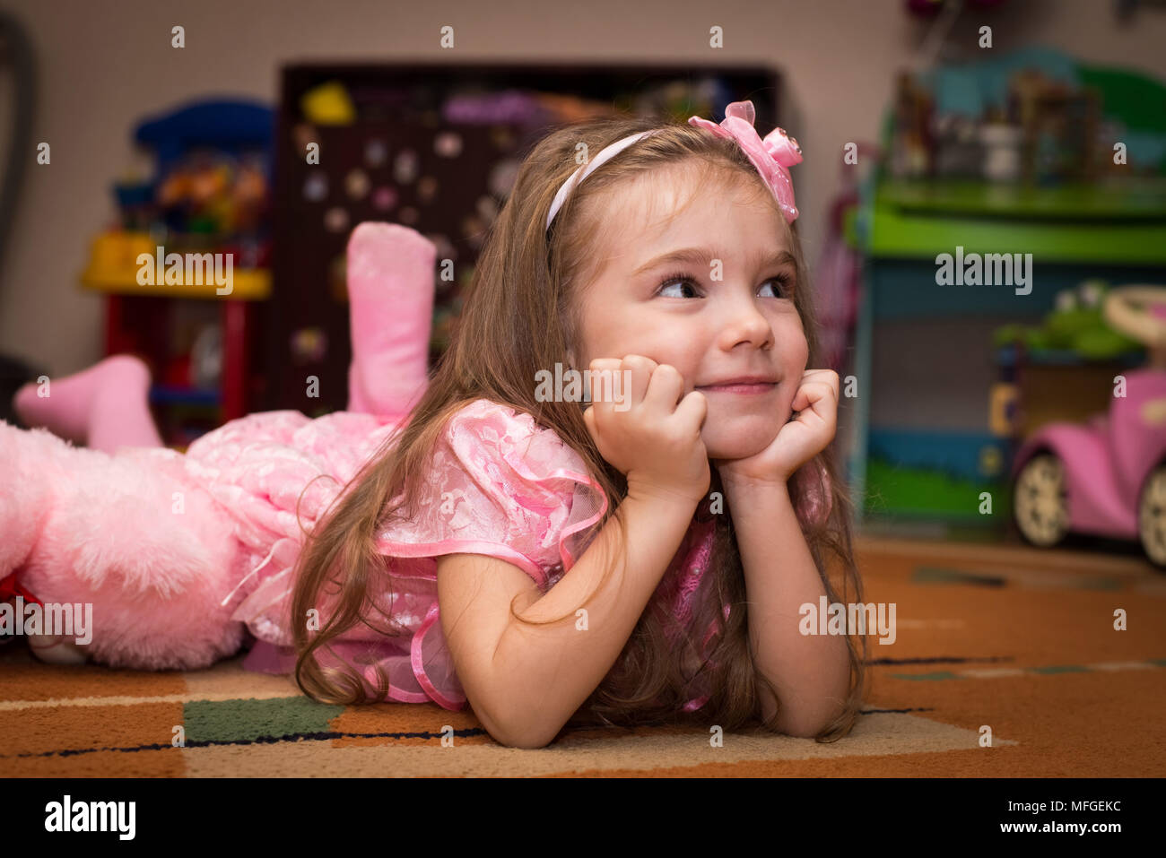 Petite fille dans une robe rose se trouve sur le sol avec un jouet Banque D'Images