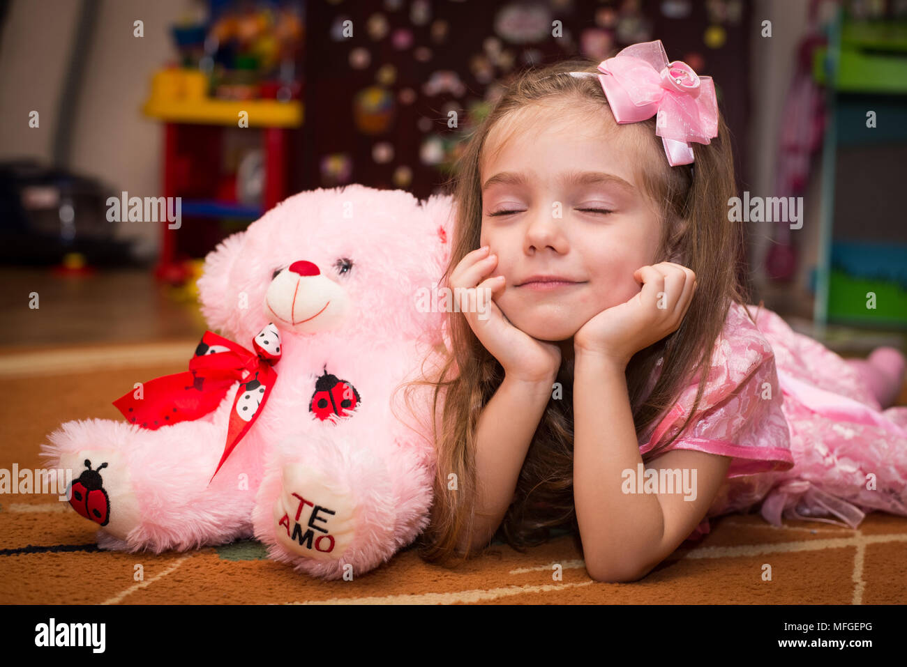 Petite fille dans une robe rose se trouve sur le sol avec un jouet Banque D'Images