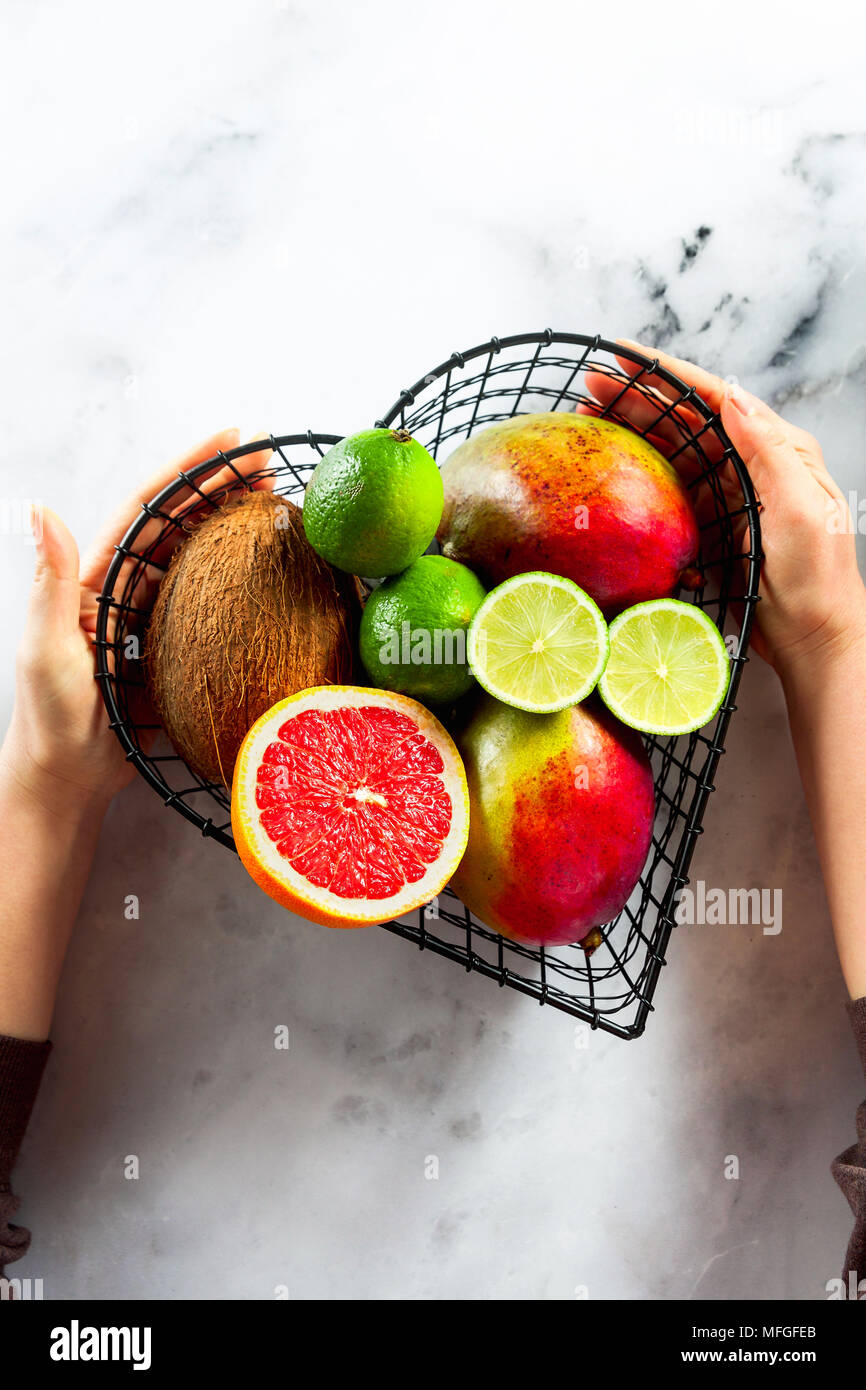 Les mains tiennent un panier sous la forme d'un coeur avec des fruits exotiques . Photo de dessus. copier l'espace. sur une table de marbre blanc Banque D'Images