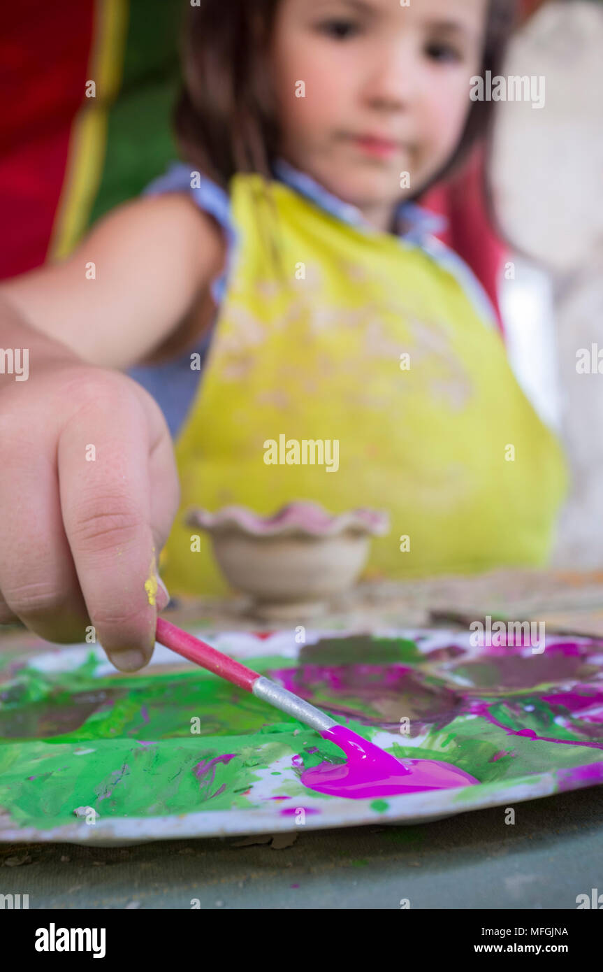 Fille enfant chargement avec sa couleur pourpre d'un pinceau. Atelier de céramique pour les enfants concept Banque D'Images