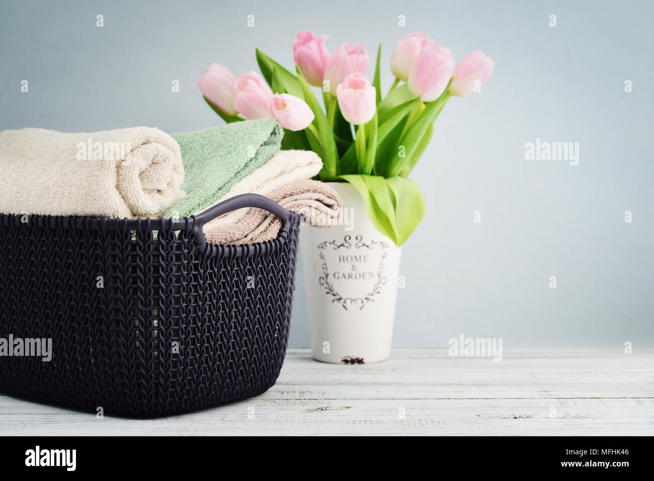 Les serviettes de bain de différentes couleurs dans panier en osier avec des tulipes dans un vase sur un fond clair Banque D'Images