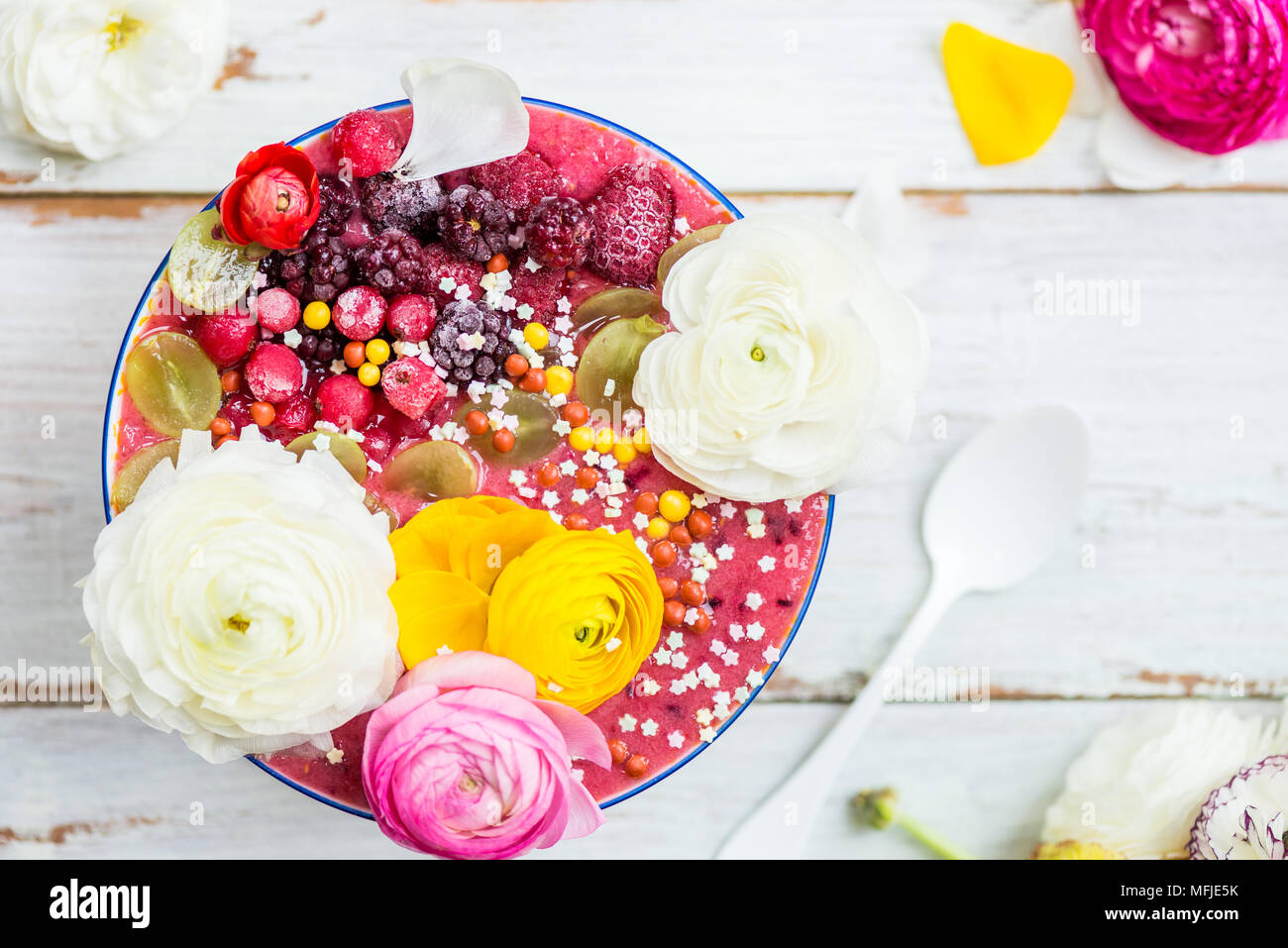 Petit déjeuner Smoothie Rose Detox à partir de la banane et de baies sauvages dans le bol, garni de petits fruits surgelés et ranunculus fleurs, un parquet en bois clair, d'arrière-plan Banque D'Images
