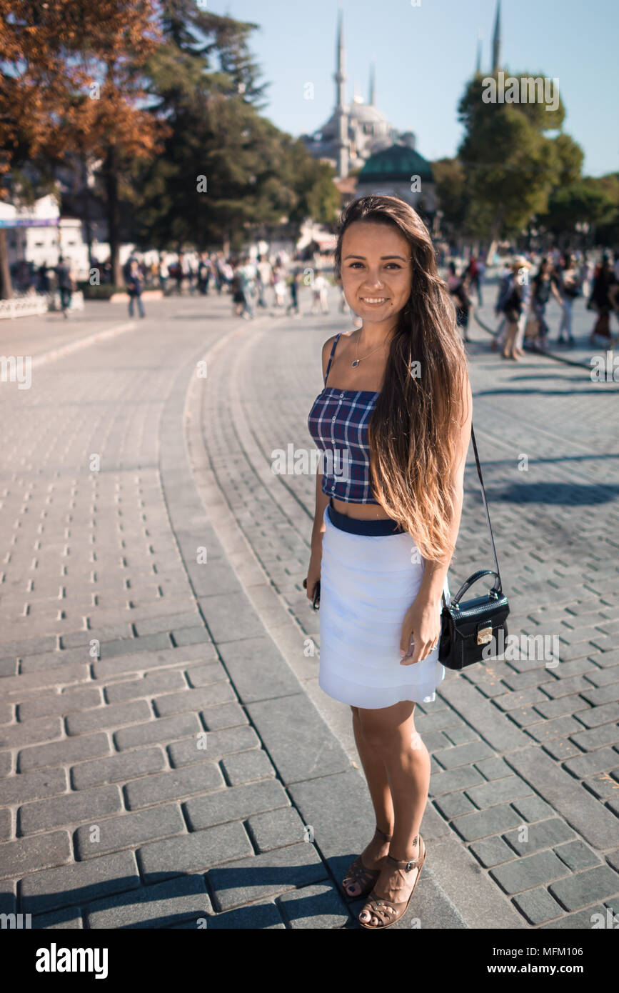 Young smiling woman stand au carré sur fond de mosquée et arbres, été journée ensoleillée. Jolie fille avec de longs cheveux bénéficie d'Istanbul en vacances Banque D'Images