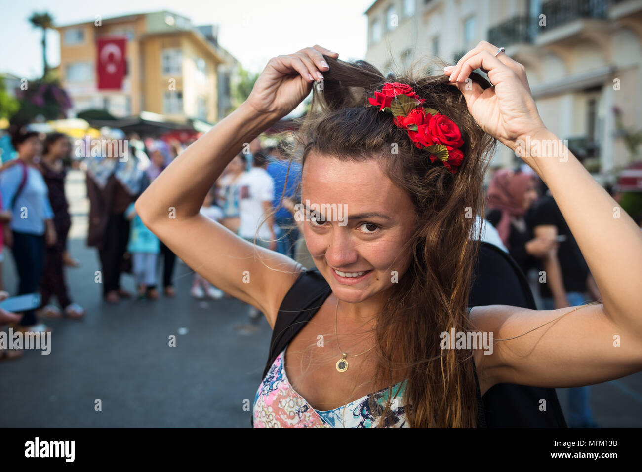 Jeune femme drôle avec des roses dans les cheveux se tient sur la place de la ville et corrige la coiffure. Confus fille sur fond de groupe de personnes. Banque D'Images