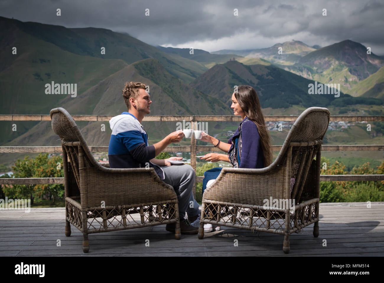 Jeune couple dans la bonne humeur est assis sur la terrasse avec des tasses de café le matin avec vue magnifique sur les montagnes. Jolie fille avec petit ami avoir briser Banque D'Images