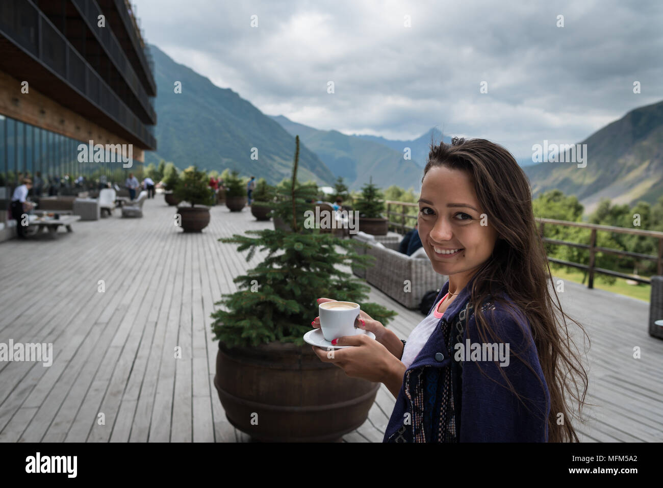 Jeune femme heureuse se tient sur la terrasse de l'hôtel avec tasse de café le matin. Belle fille de bonne humeur et est prêt pour l'aventure. Banque D'Images