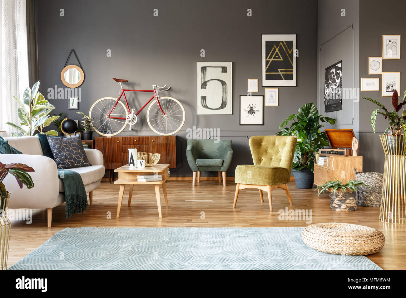 Pouf sur tapis gris en grand salon intérieur avec des fauteuils verts, affiches et red bike Banque D'Images