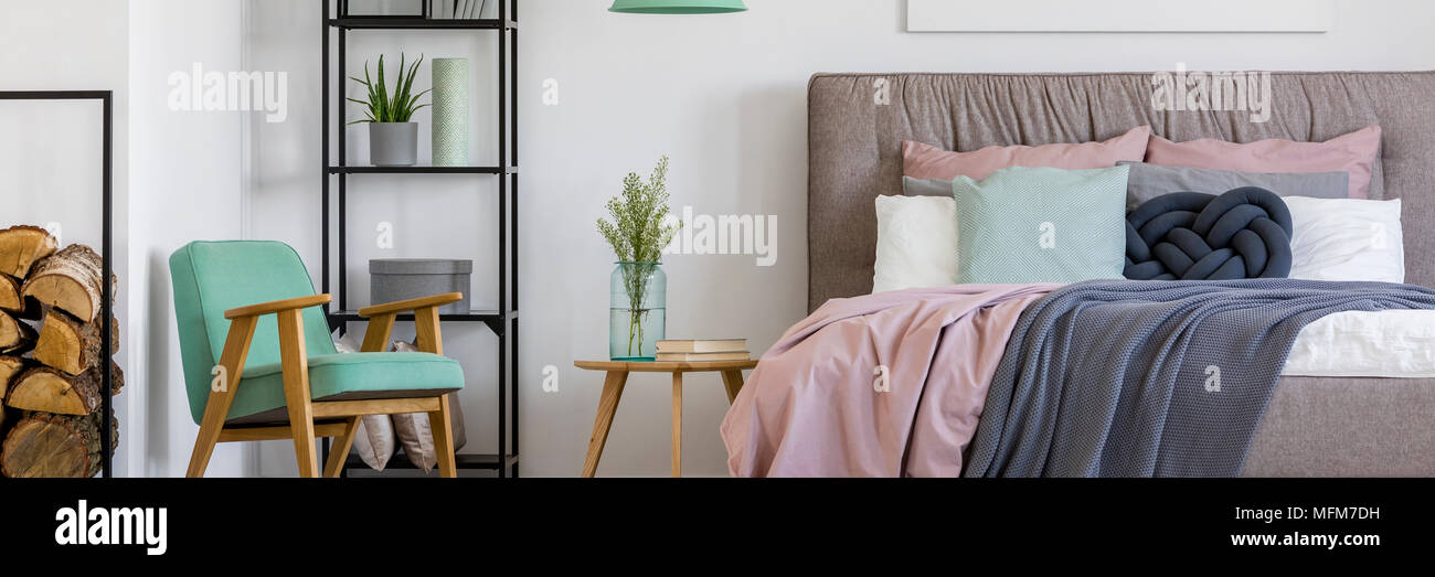 Confortable, chambre scandinaves intérieur pour une femme avec une décoration en bois, fauteuil de menthe, une étagère, des plantes et des coussins sur un grand lit Banque D'Images