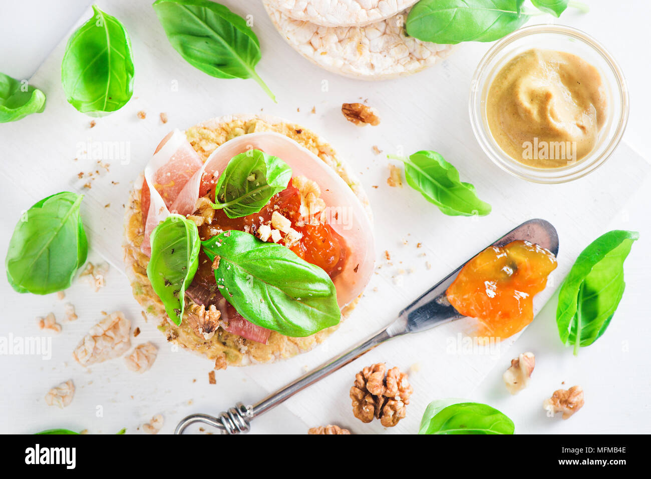 Pain croustillant collation santé avec jambon de Parme, noix, moutarde, confiture d'abricot, de feuilles de basilic frais. Petit-déjeuner facile gros plan sur un fond blanc avec copie s Banque D'Images