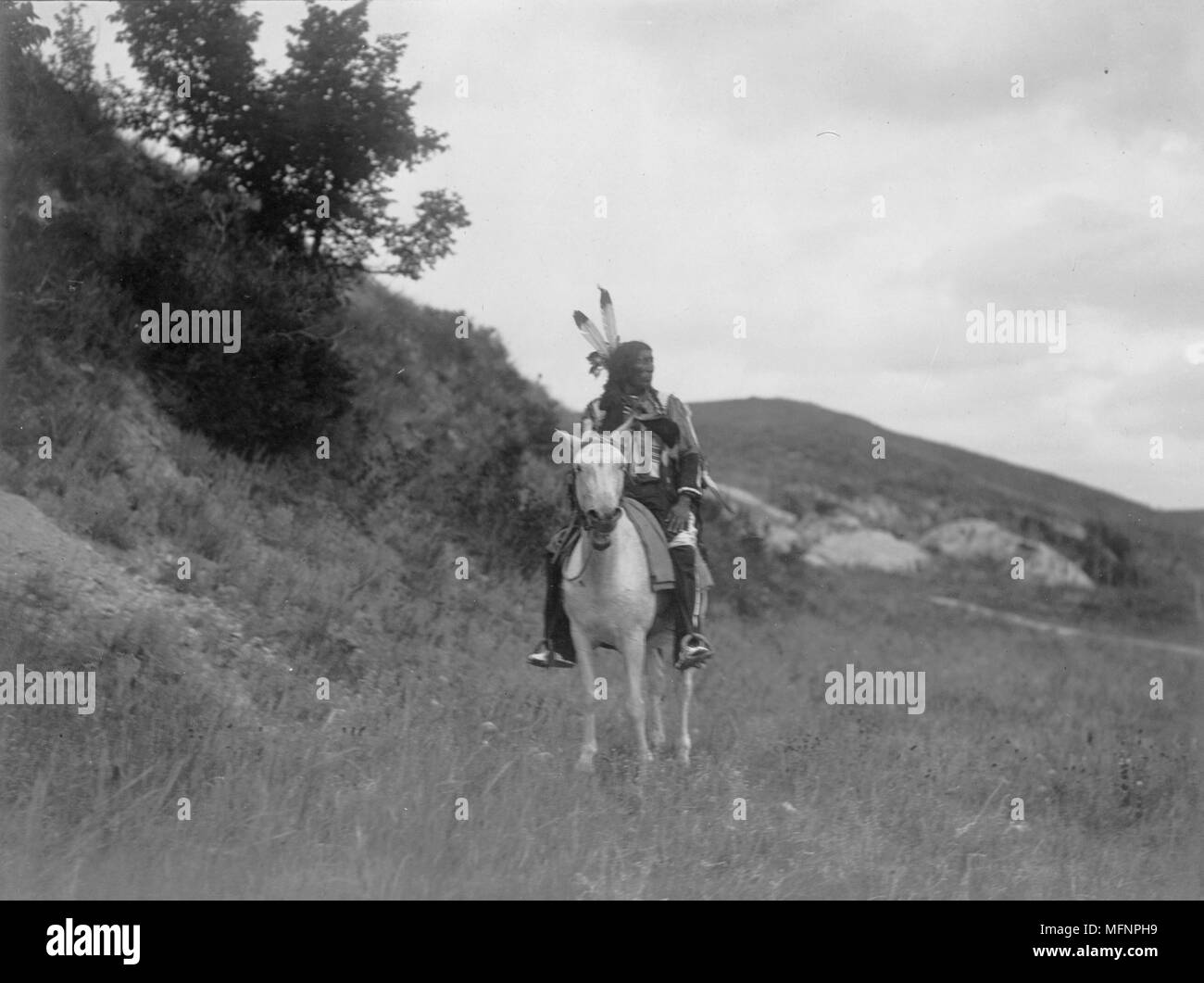 Les Indiens Sioux à cheval, portant deux plumes, robe chemise en peau de daim, et des jambières, collines en arrière-plan, c1907. Photographie, Edward Curtis (1868-1952). Banque D'Images