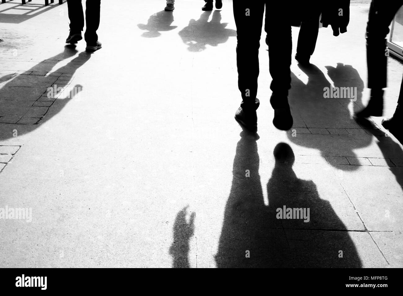 Ombres et silhouettes de personnes marchant sur le trottoir de la ville tôt le matin dans le noir et blanc Banque D'Images