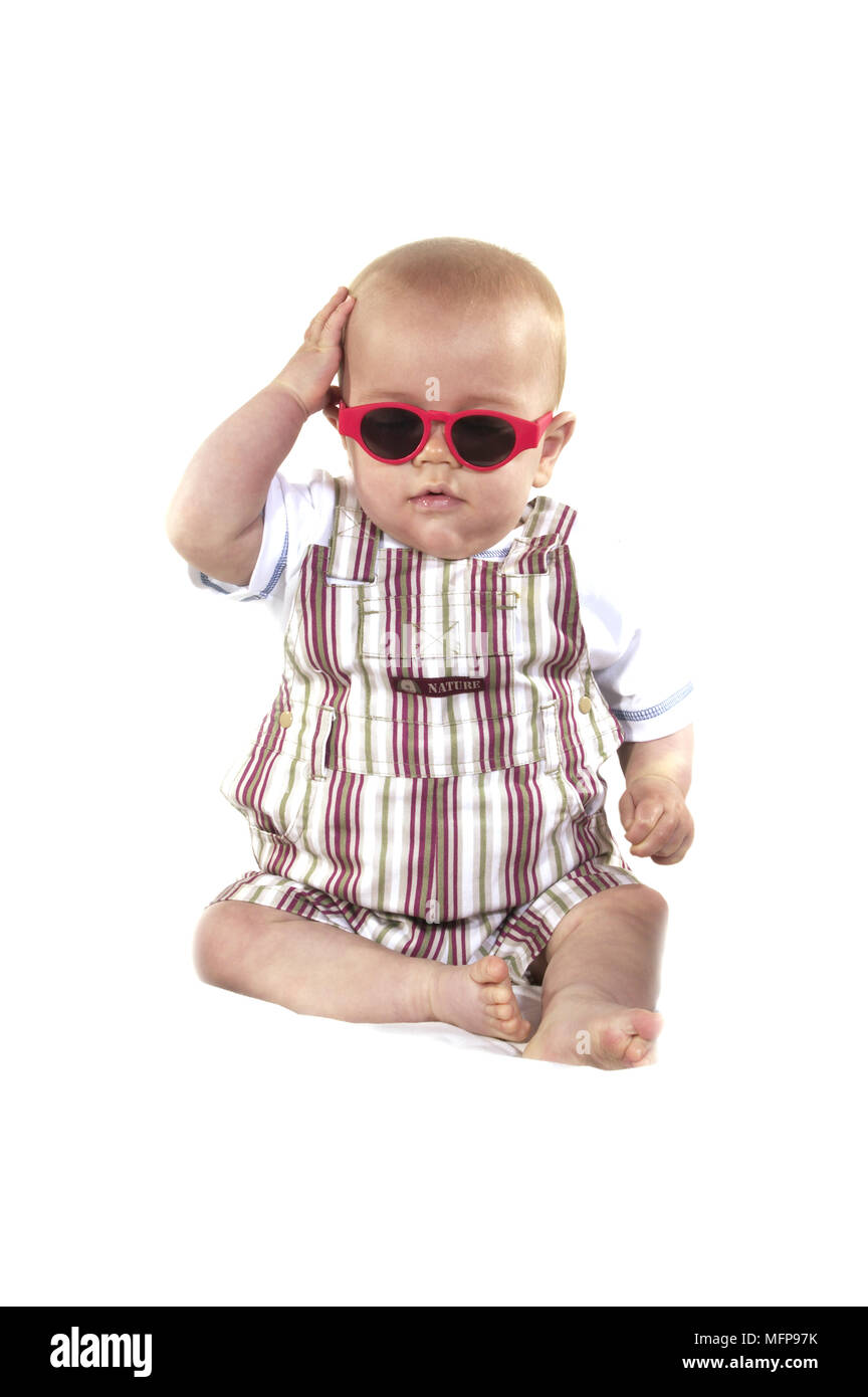 Bébé Garçon avec des lunettes de soleil assis contre fond blanc Banque D'Images