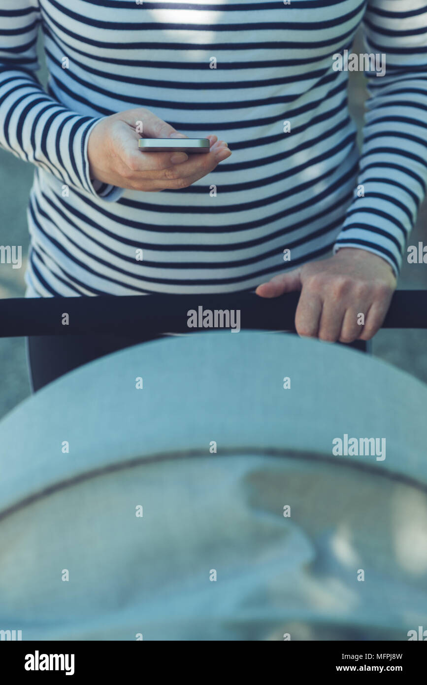 Mère à l'aide de téléphone mobile tout en poussant la poussette de bébé dans la rue, selective focus Banque D'Images