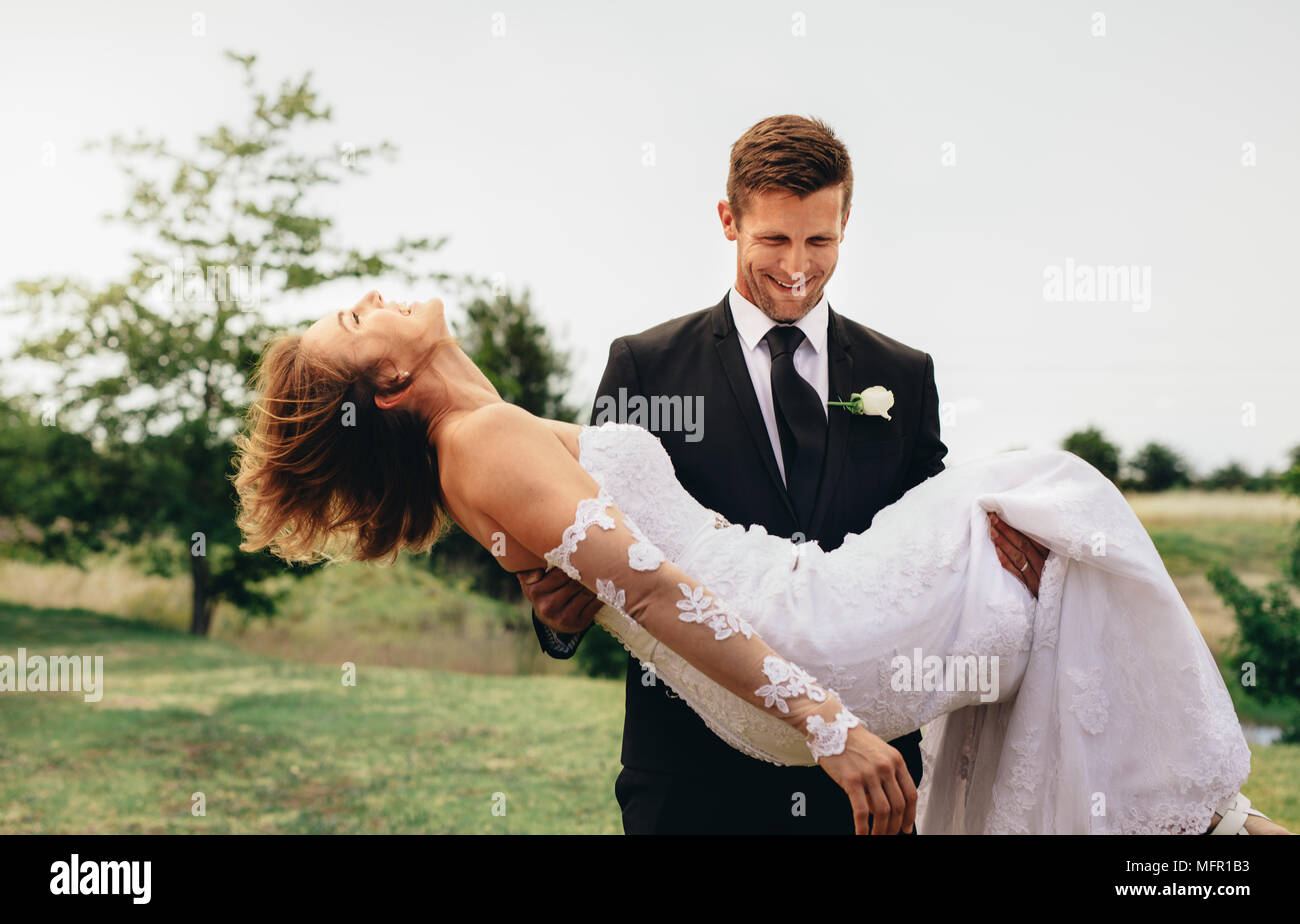 Groom Smiling bride comptable sur les armes au parc. Beautiful wedding couple avec groom soulevant sa mariée et la marche à pied. Banque D'Images Groom Smiling bride comptable sur les armes au parc. Beautiful wedding couple avec groom soulevant sa mariée et la marche à pied. Banque D'Images