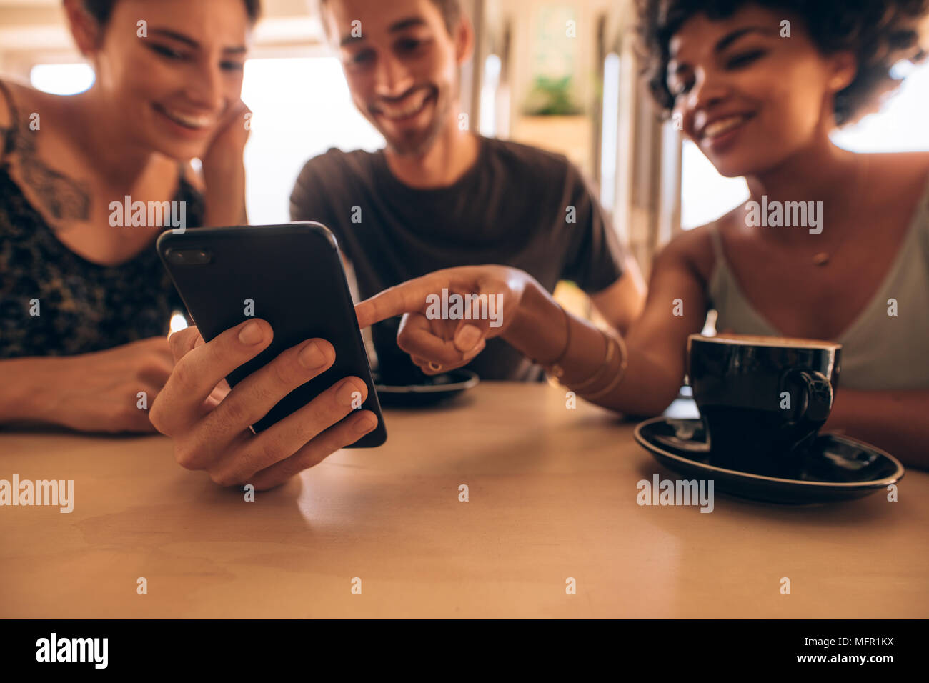 Groupe d'amis réunis au café et à la recherche sur téléphone mobile. Homme montrant son téléphone à des amis avec une femme pointant à l'écran mobile. Banque D'Images