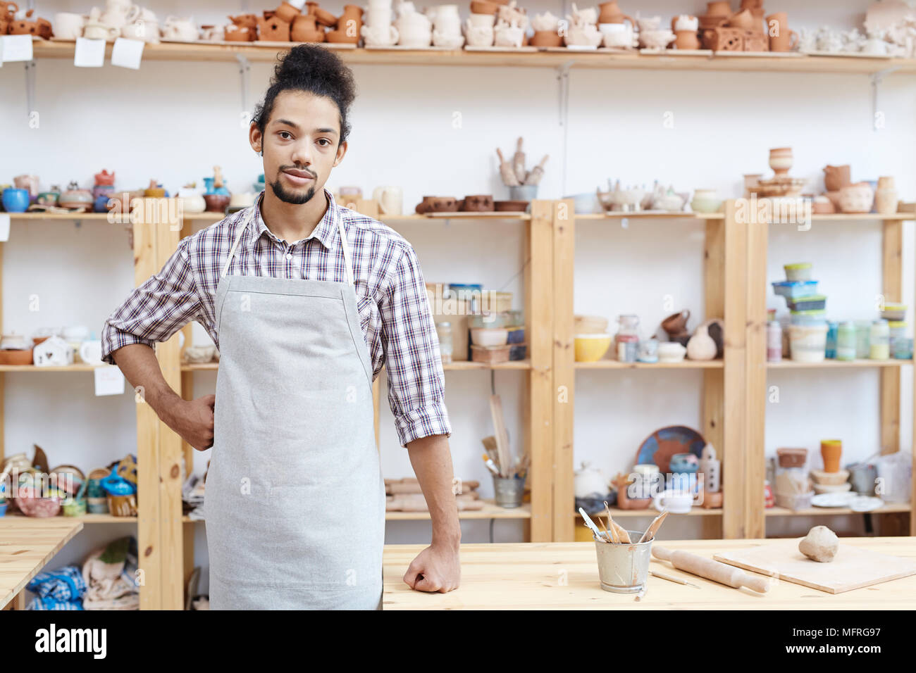 Portrait de jeune homme en tablier, debout dans l'atelier avec des produits d'argile et looking at camera Banque D'Images