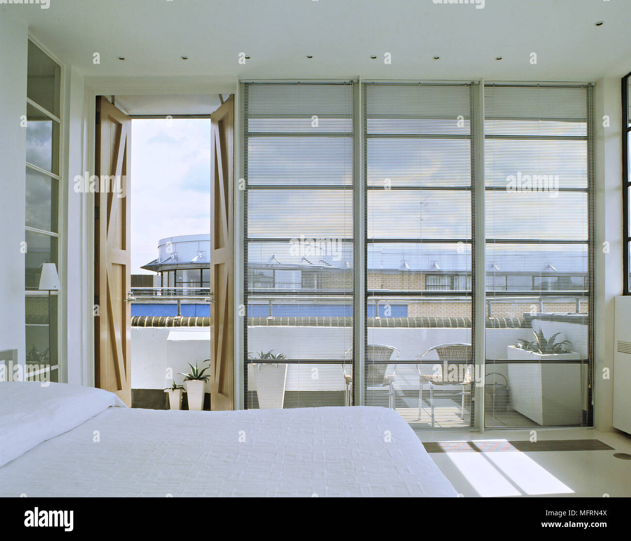 Un détail d'un blanc minimaliste moderne chambre à coucher avec lit double fenêtre du sol au plafond, porte ouverte sur balcon salon Banque D'Images