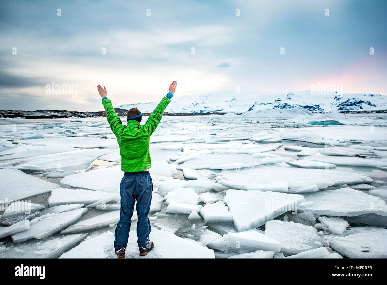 Hiker holding ses mains en l'air, debout sur un banc de glace, glacier Jökulsárlón Lagoon, lac glaciaire, coucher du soleil Banque D'Images