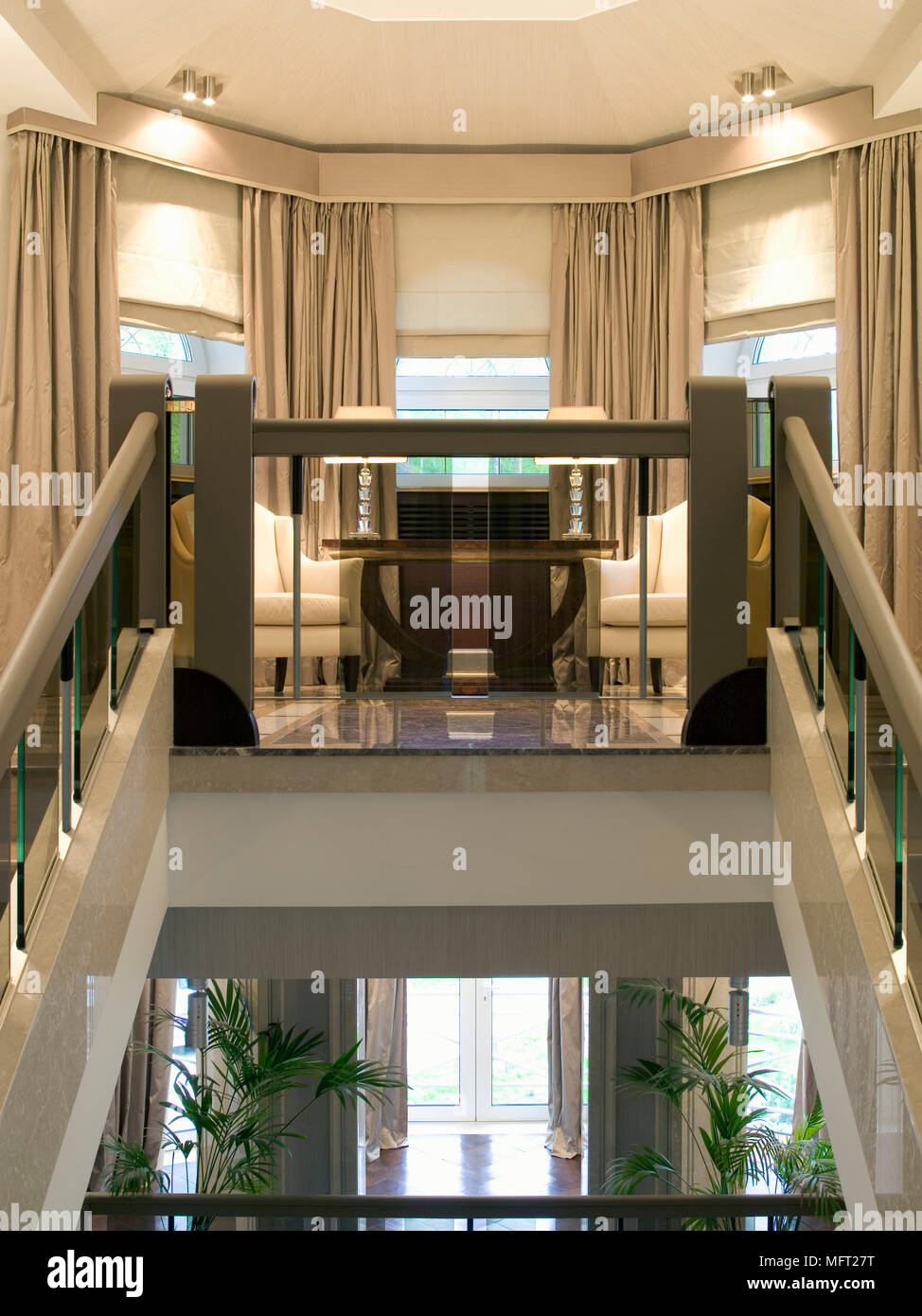 Rampes en verre menant à l'atterrissage avec des fauteuils au-dessus de la porte flanquée de plantes Banque D'Images