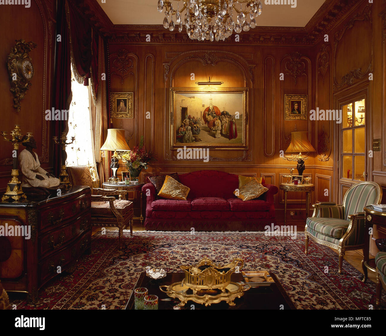 Salon traditionnel avec des murs lambrissés, tapis orientaux, canapé de velours, et lustre en cristal. Banque D'Images