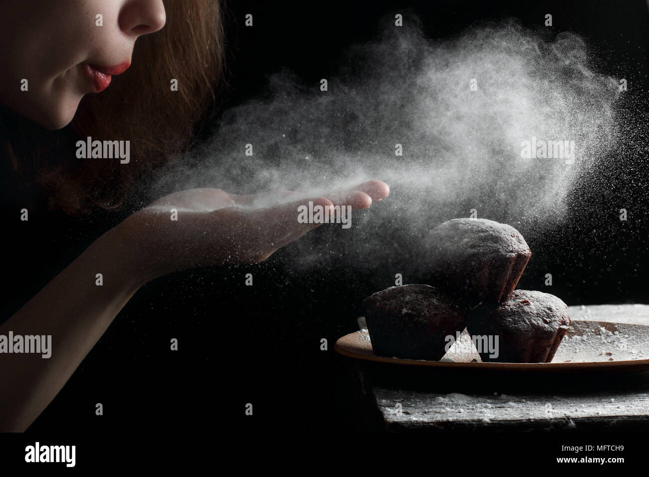 Soufflé de sucre en poudre avec les mains sur les muffins, photographiés avec la lumière d'un flash Banque D'Images