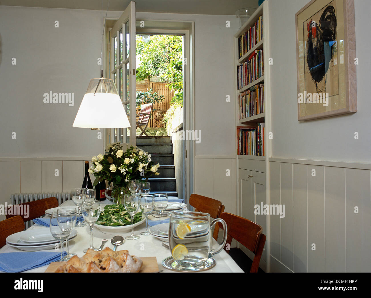 Vue d'un pays à manger avec un set de table pour le déjeuner, une lampe, photo sur le mur, une étagère et une porte ouverte donnant sur un jardin. Banque D'Images