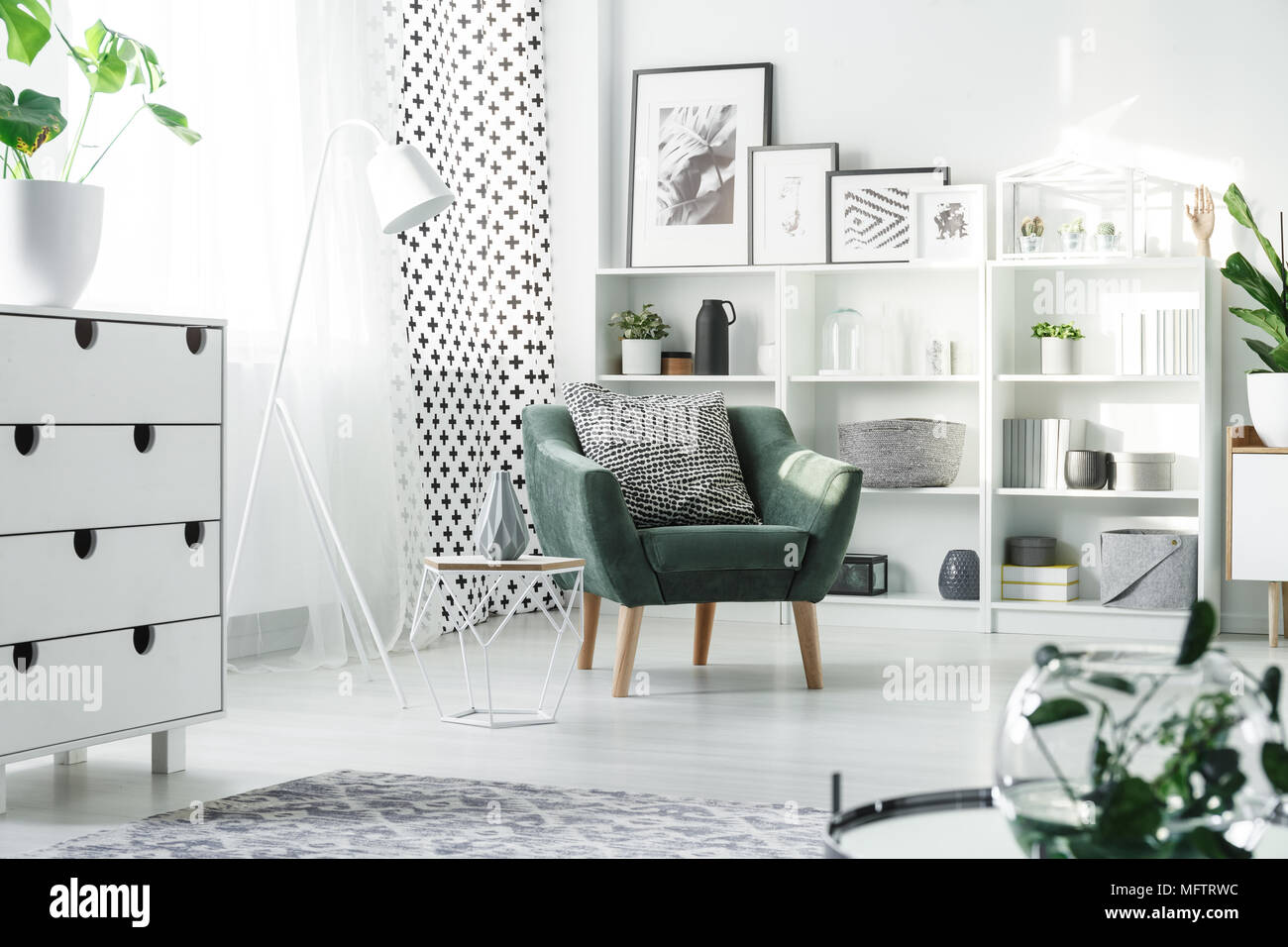 Le mobilier blanc et vert fauteuil avec coussin à motifs placés dans des studio intérieur avec fenêtre et affiches Banque D'Images
