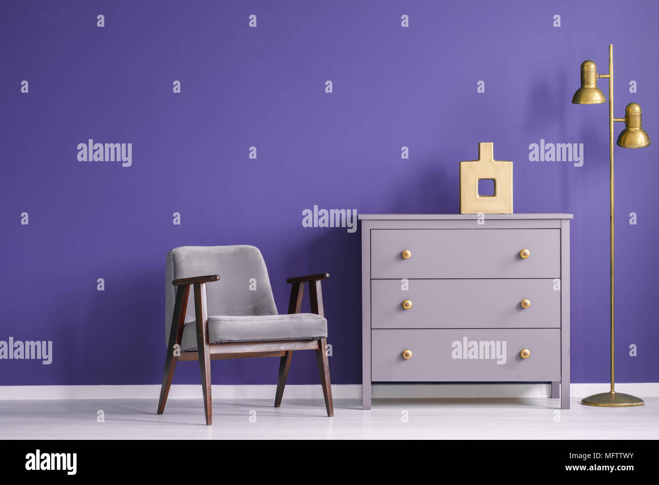 Salon ultra violet rétro intérieur avec un fauteuil et une commode à côté d'une lampe d'or. Photo réelle. Banque D'Images