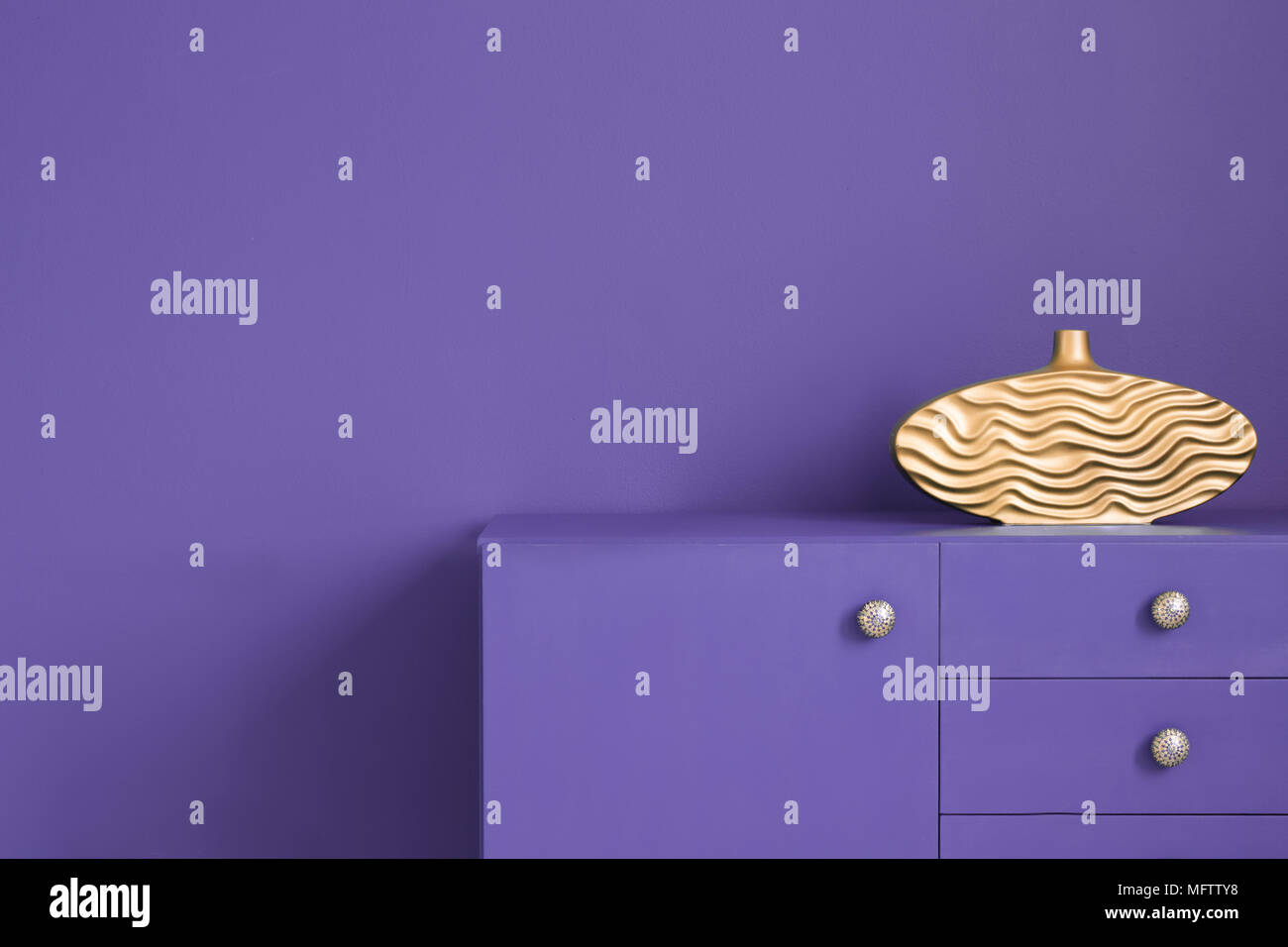 Gros plan d'un mur et d'un ultra violet cabinet correspondant avec un vase d'or sur le dessus dans un intérieur créatif. Photo réelle Banque D'Images