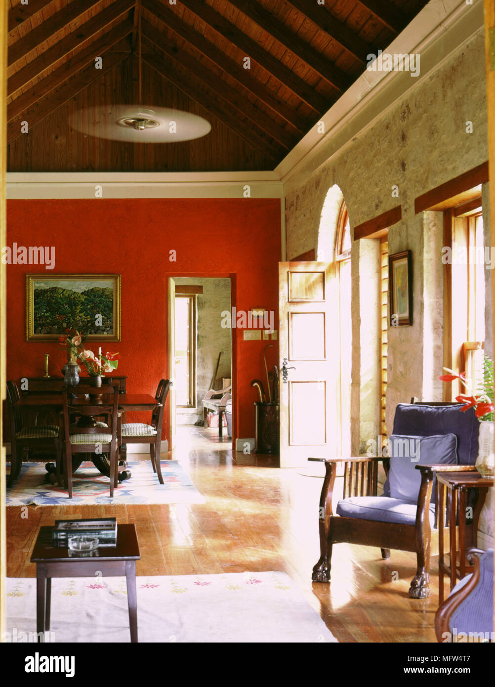 Salon avec un toit en pente de murs en pierre d''une table à manger et chaises et fauteuils en bois d'une terrasse bien porte ouverte. Banque D'Images