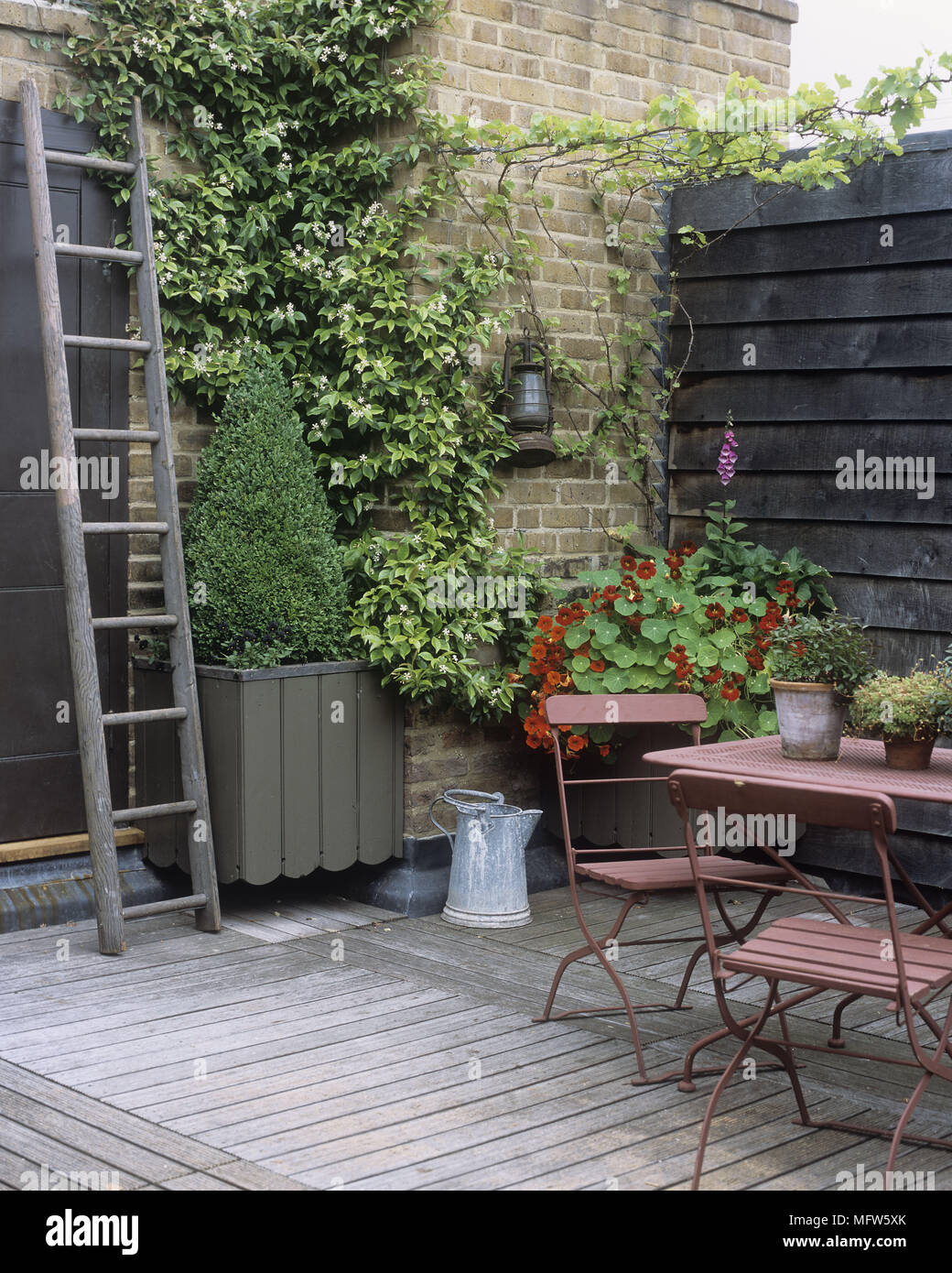Un patio extérieur table et chaises de jardin sur un patio en bois avec des plantes d'une échelle et de plantes en pot. Banque D'Images