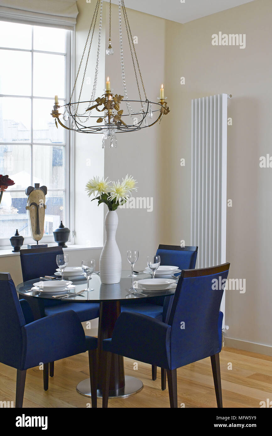 De confortables chaises bleu autour d'une table à manger près d'une fenêtre avec un lustre et un radiateur mural. Banque D'Images