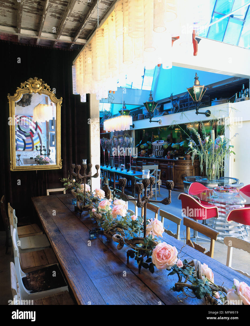 Détails d'une grande salle à manger dans un restaurant au style bohème avec un miroir derrière une longue table en bois avec une longue rangée de fleurs décoratives. Banque D'Images