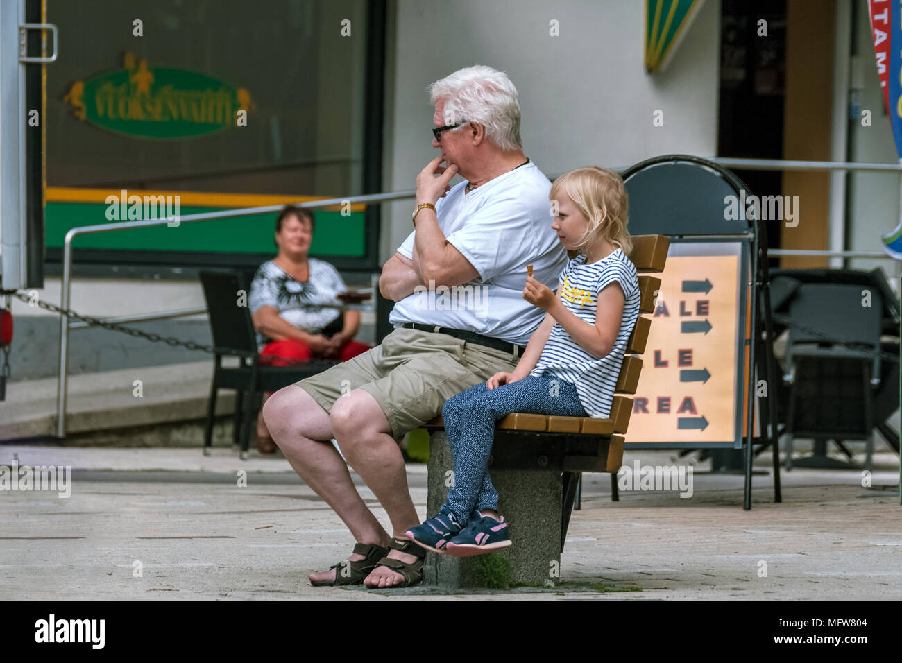 Imatra, Finlande, Juin 24 : Un homme âgé avec des lunettes et une petite fille avec de la crème glacée, assis sur un banc dans le centre de la ville finlandaise d'Imatra Banque D'Images