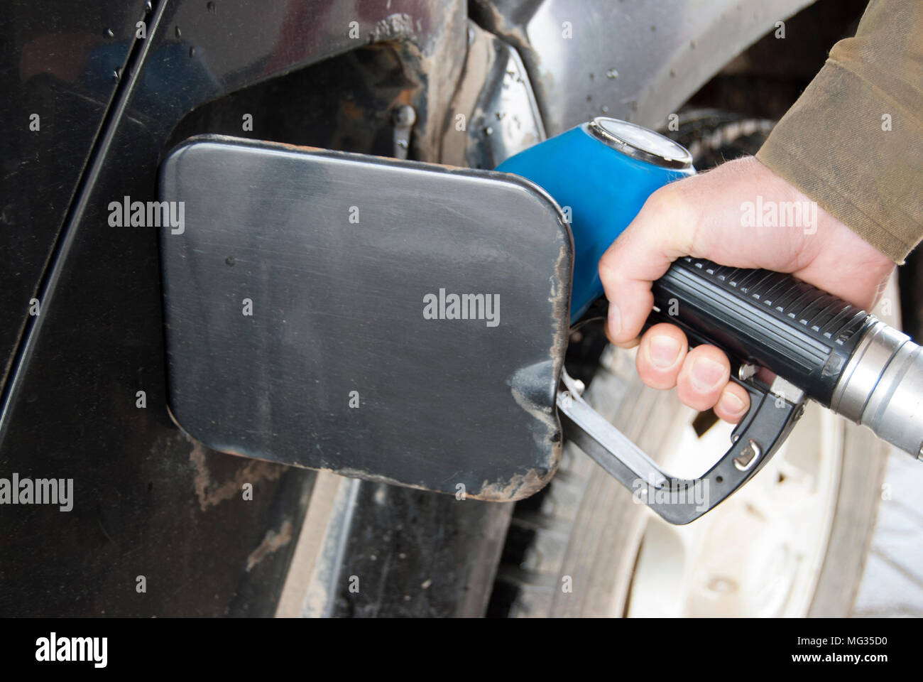 Une main d'homme est titulaire d'un pistolet de ravitaillement dans une station d'essence et exécute une vieille voiture sale. Banque D'Images