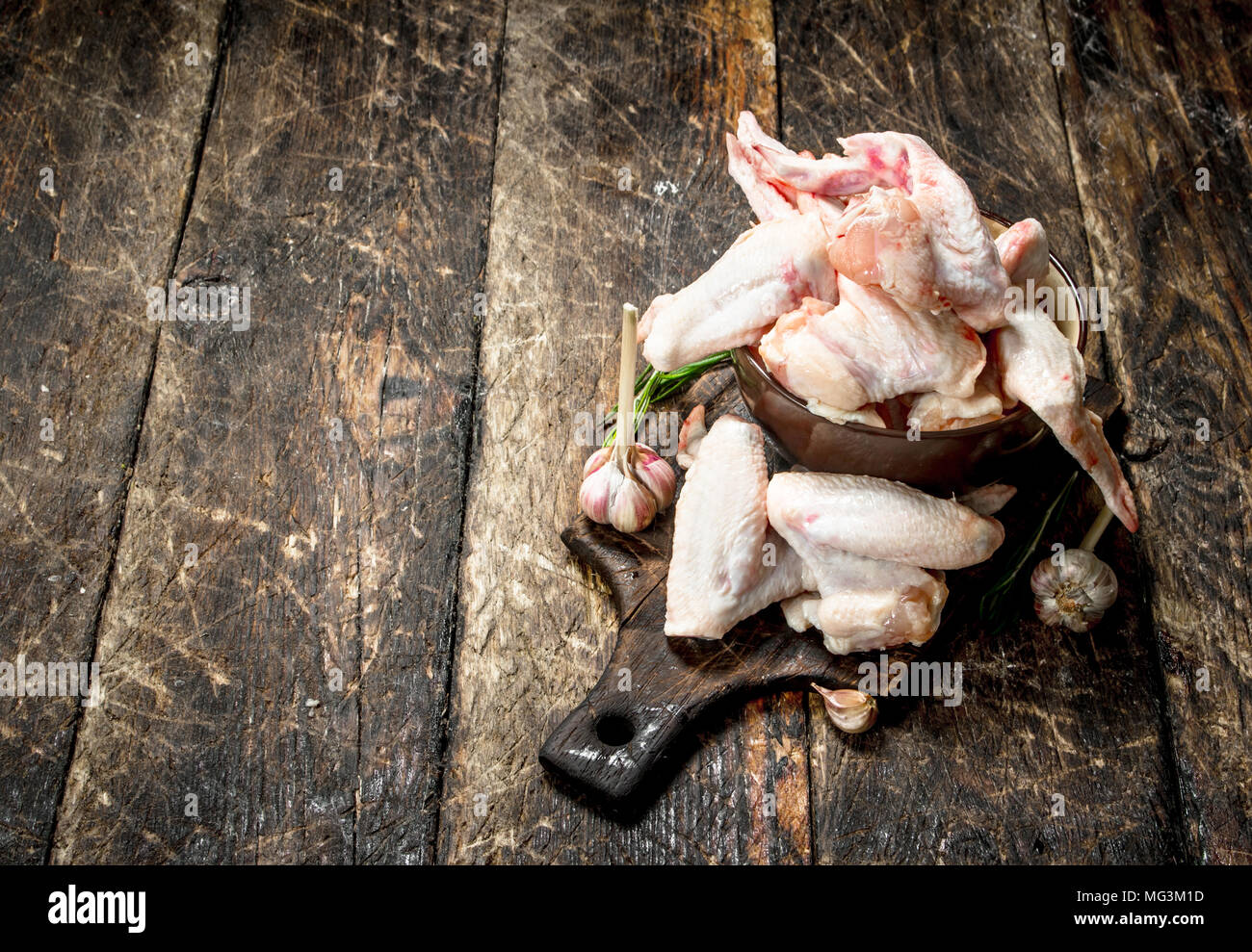 Ailes de poulet crues avec l'ail et fines herbes dans un bol . Sur fond de bois. Banque D'Images