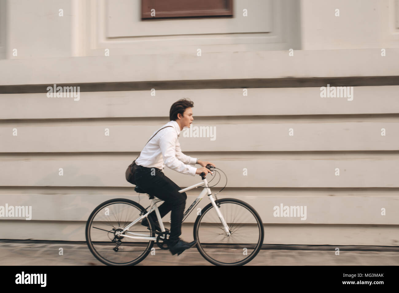 Dépêchez-Asian businessman riding bike en heure de pointe. Jeune homme en retard pour le travail, la réunion. La vie de bureau et la concurrence entre les entreprises. Banque D'Images