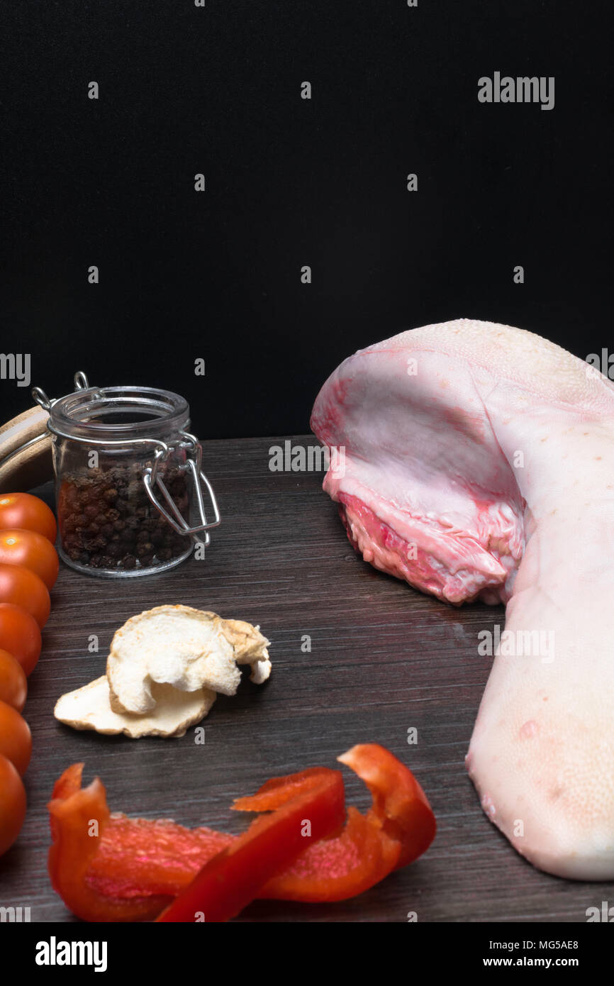 La langue de porc ou de boeuf aux légumes - le céleri, le poivre noir et rouge, l'ail, l'oignon, se trouve sur une planche à découper, sur fond noir, close-up Banque D'Images