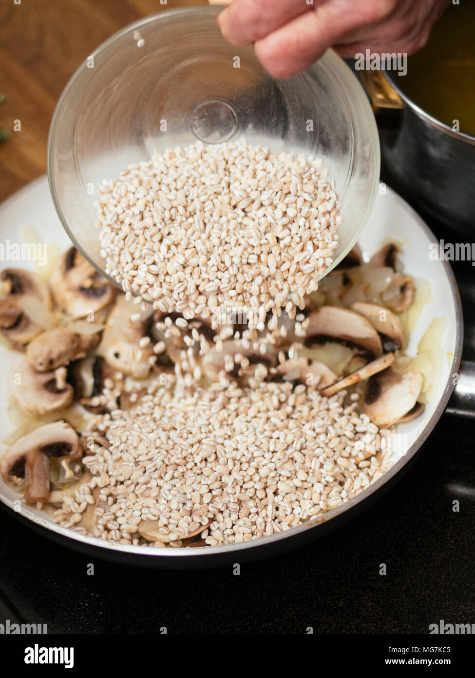 L'ajout d'un bol de cuisson de l'orge dans une poêle avec les champignons pour faire à peine risotto aux champignons. Banque D'Images