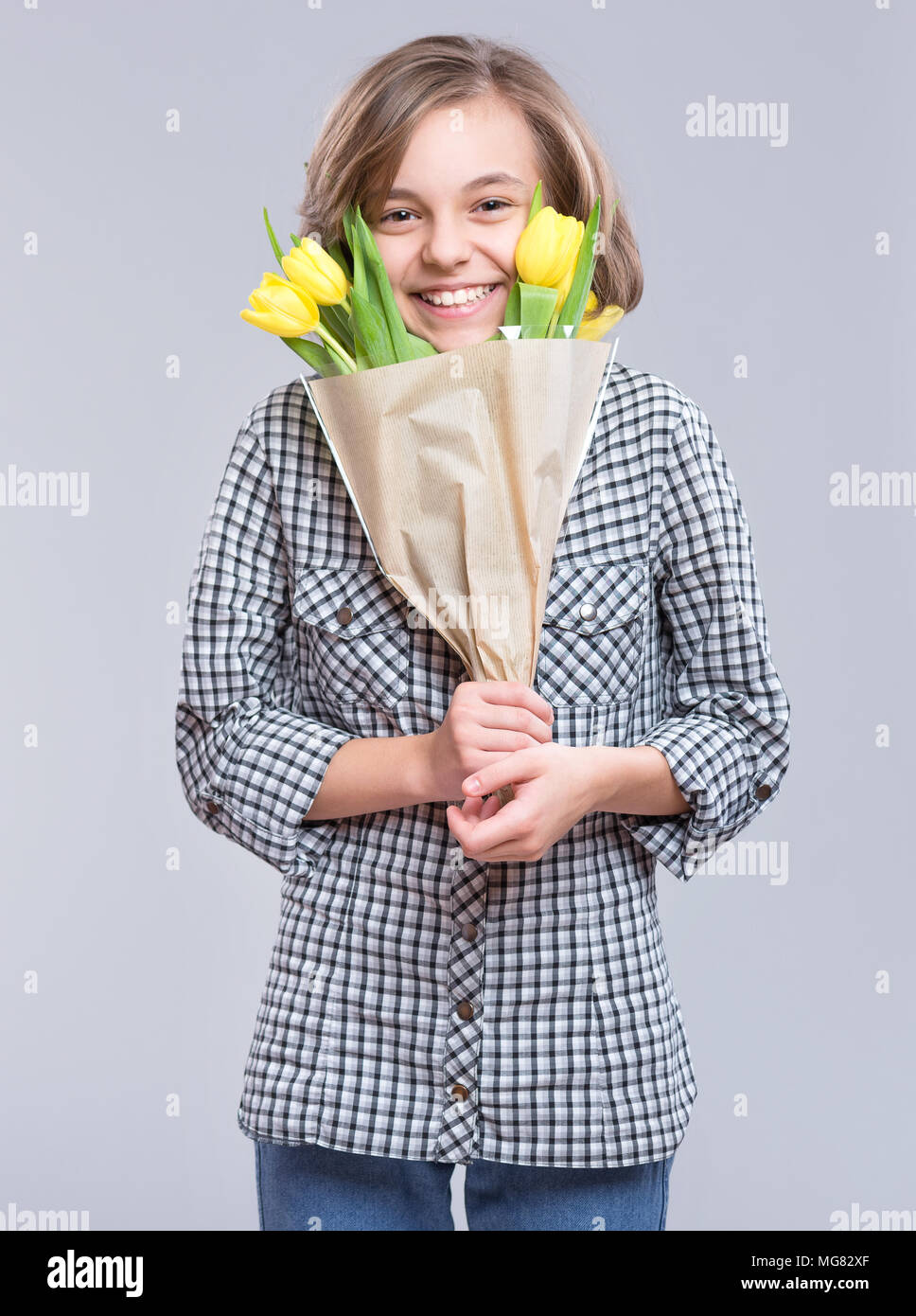 Belle jeune fille se cachant derrière bouquet de fleurs sur fond gris. Enfant avec bouquet de tulipes jaunes comme un cadeau. Heureux les mères, anniversaire ou Valen Banque D'Images