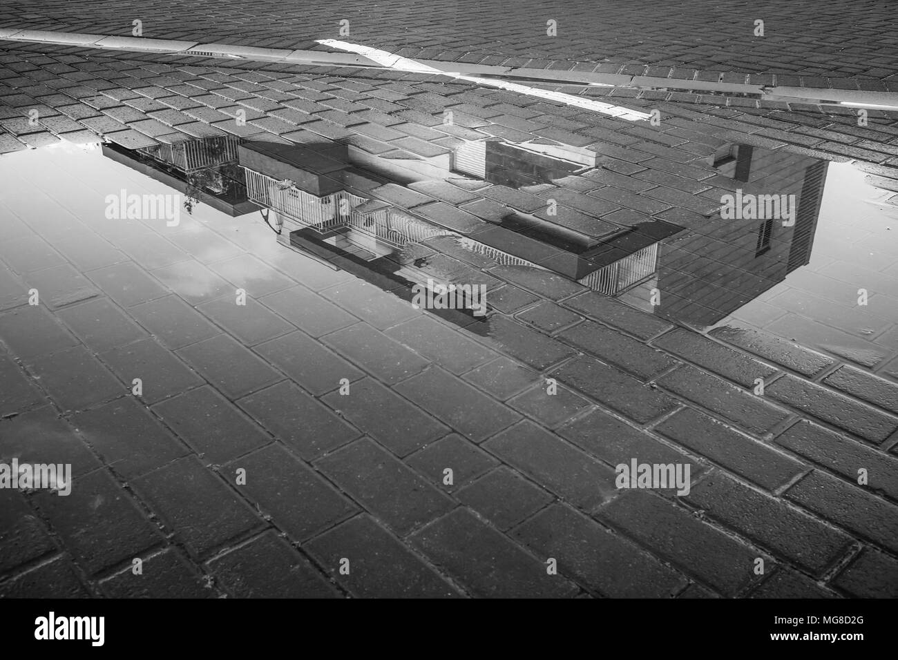 Une photographie en noir et blanc d'un bâtiment reflété dans une flaque d'eau de pluie sur un trottoir de la rue Banque D'Images