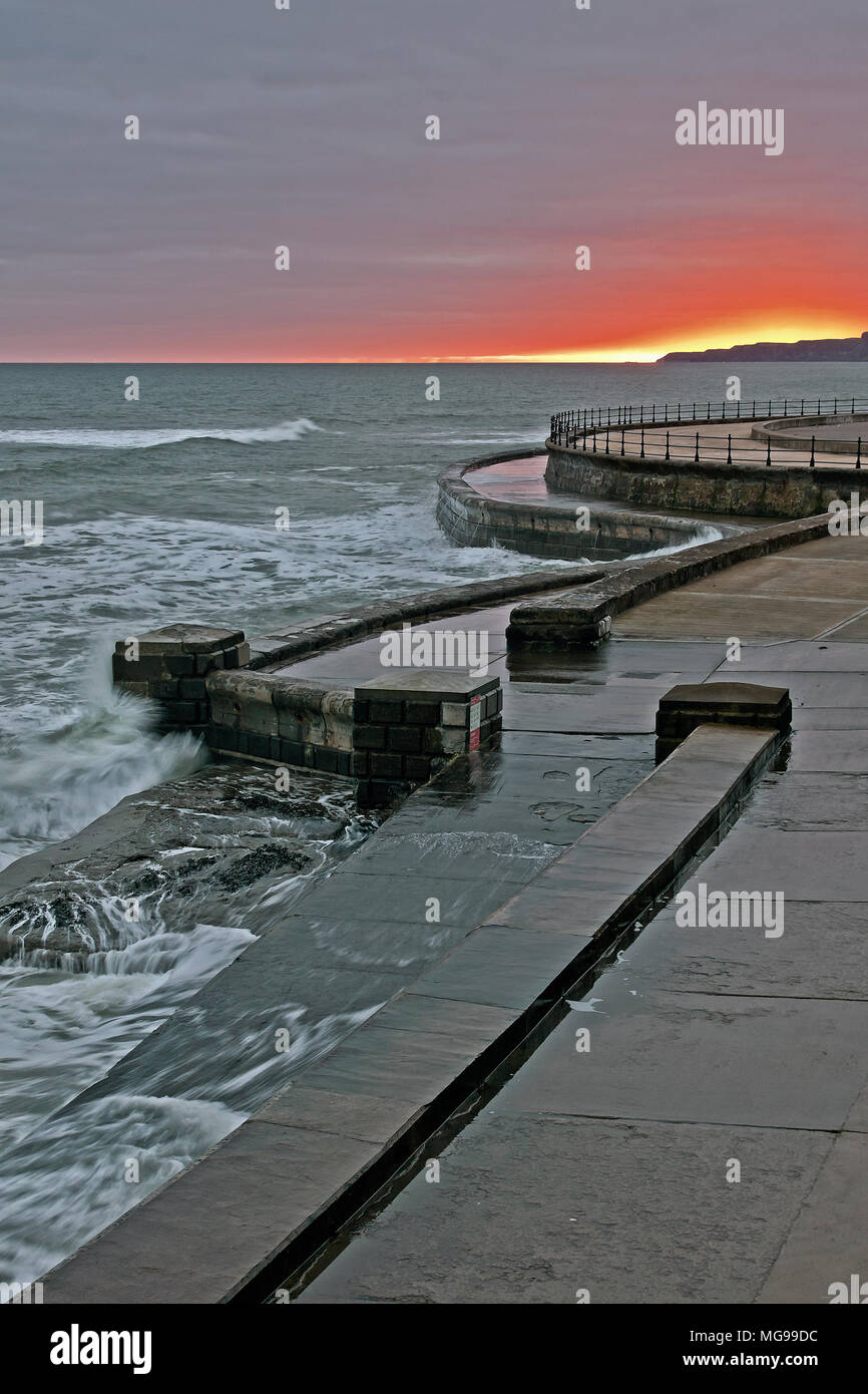 Lever du soleil à marée haute avec mer agitée se briser contre les murs et des cales de Scarborough's South Bay. Banque D'Images
