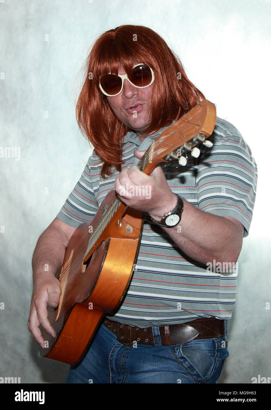 Guitariste avec longs cheveux rouges joue de la guitare et chante quelque chose. Banque D'Images